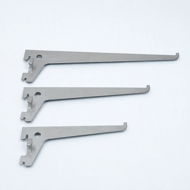 Three silver-grey wall-track shelf brackets resting flat on a pale ice-blue surface, with mounting hooks and thin metal edges visible