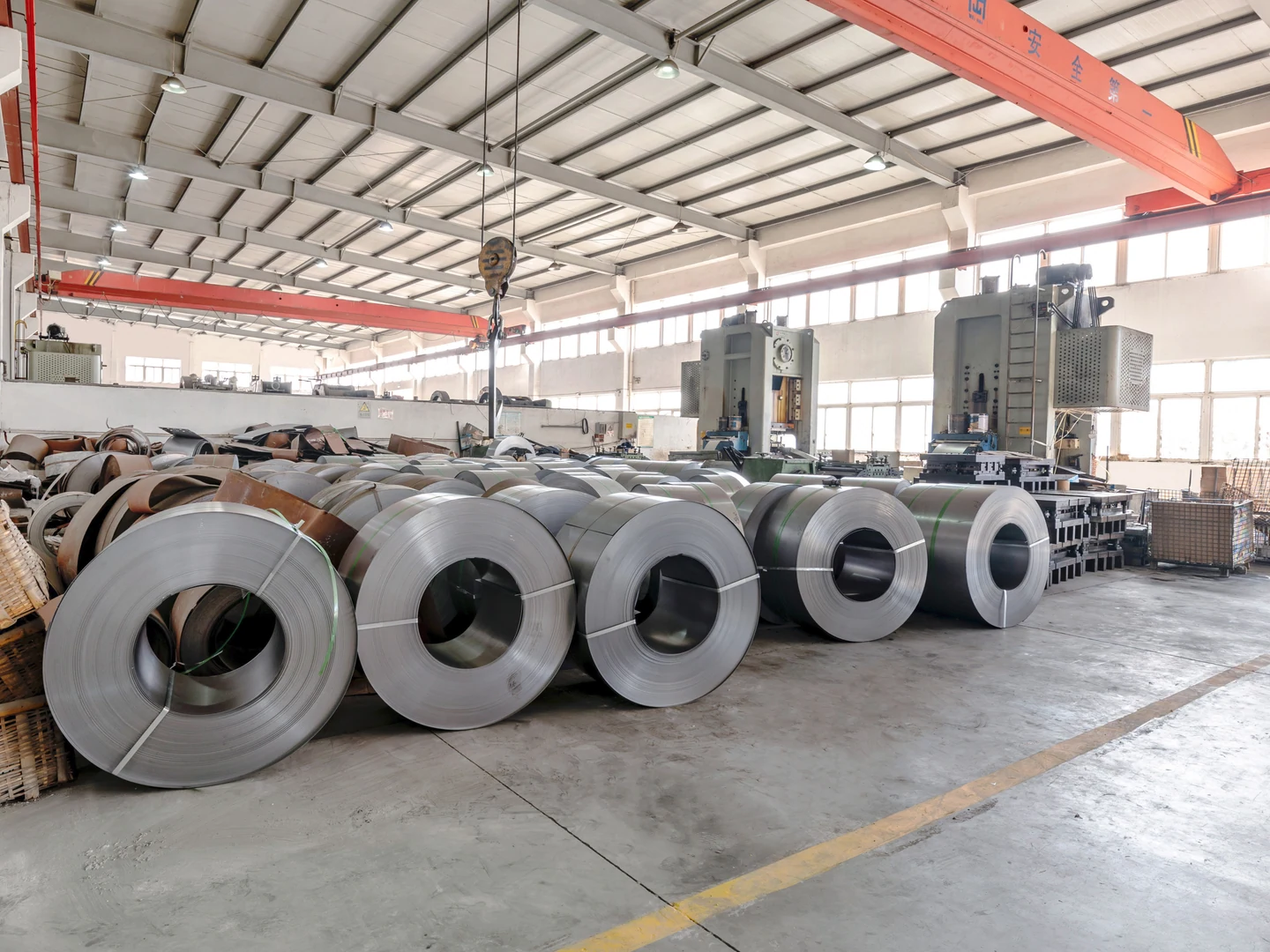Large steel coils in front of mechanical presses, tooling and an overhead crane