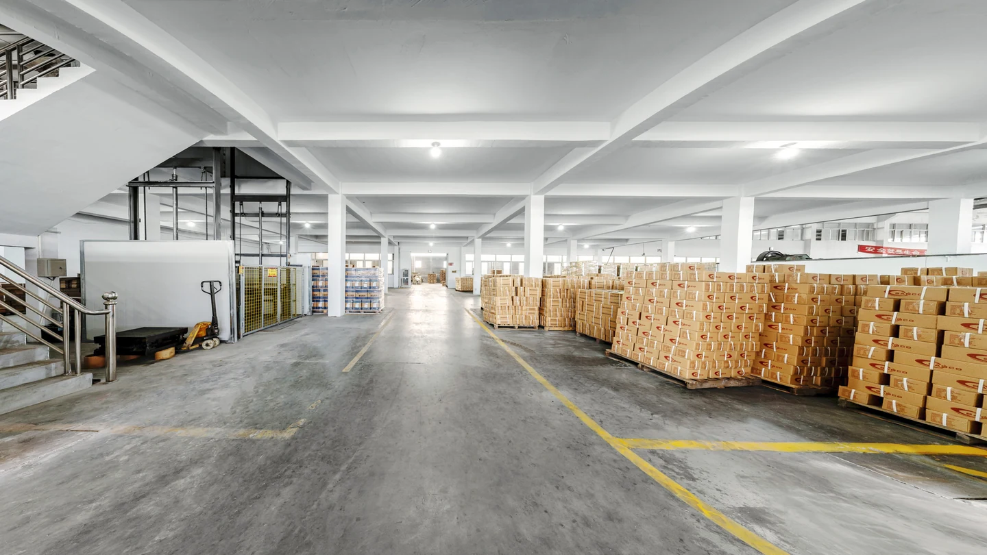 Palletized cartons beside marked access lanes, with a goods lift and pallet truck to the left