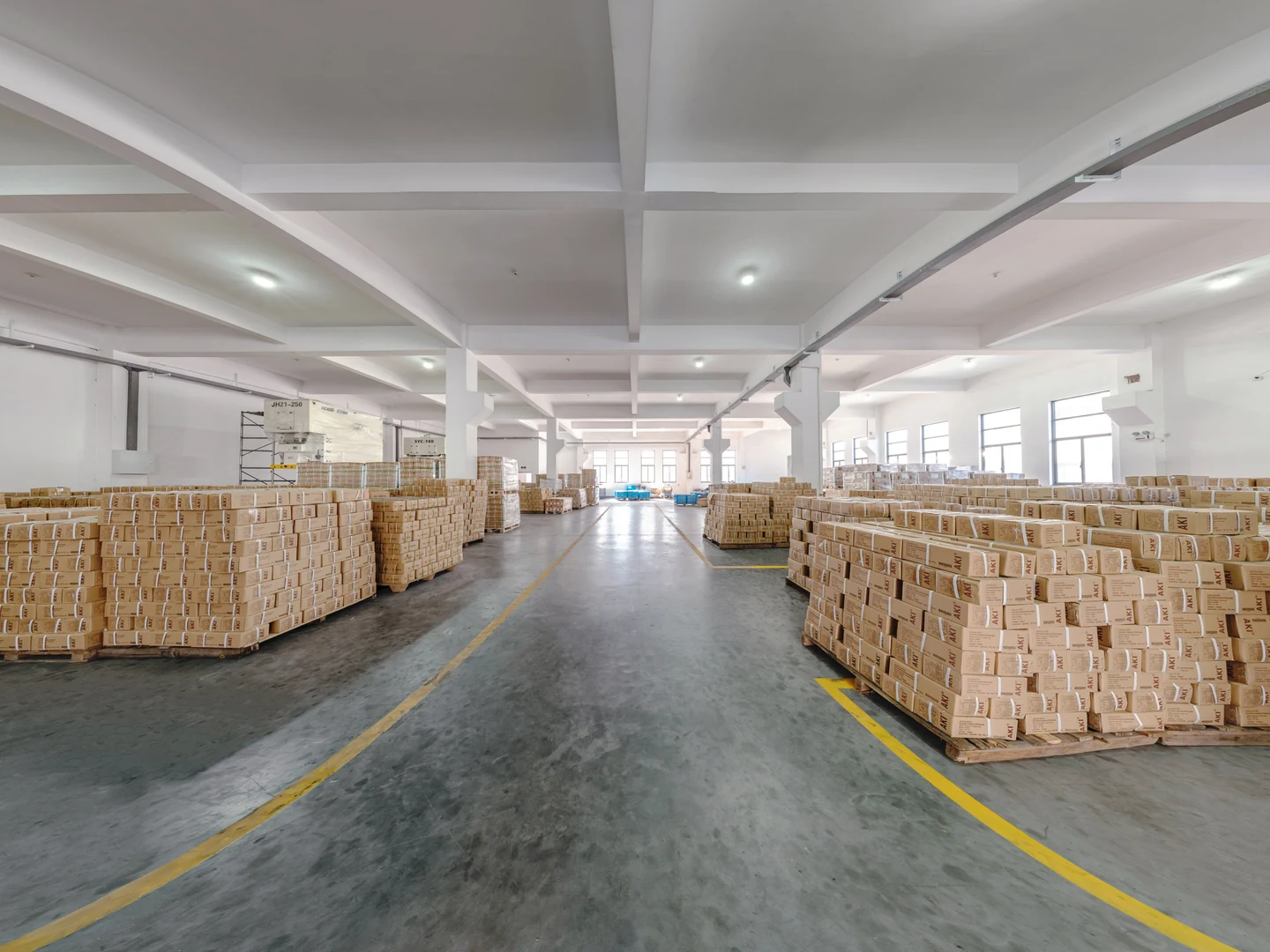 Rows of strapped cartons on pallets on both sides of a warehouse aisle marked with yellow lines